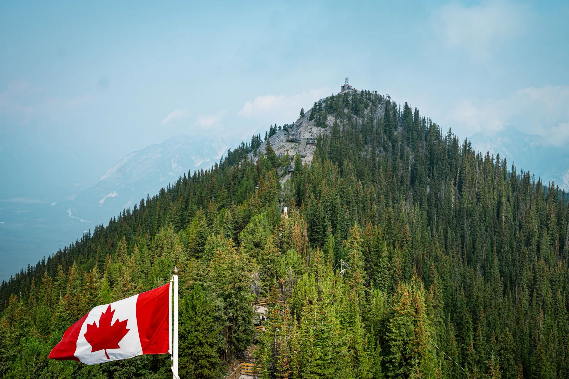 A Canadian flag in front of a forested mountain peak