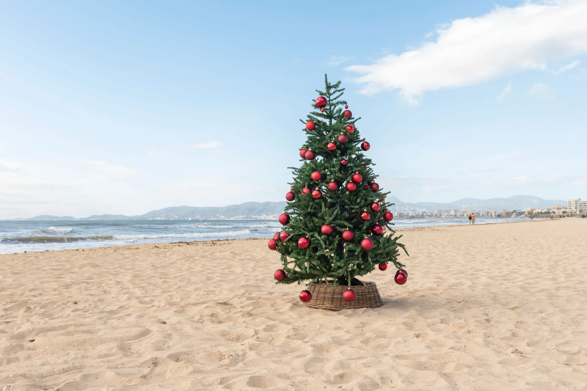 A Christmas tree with red baubles standing on a sunny beach