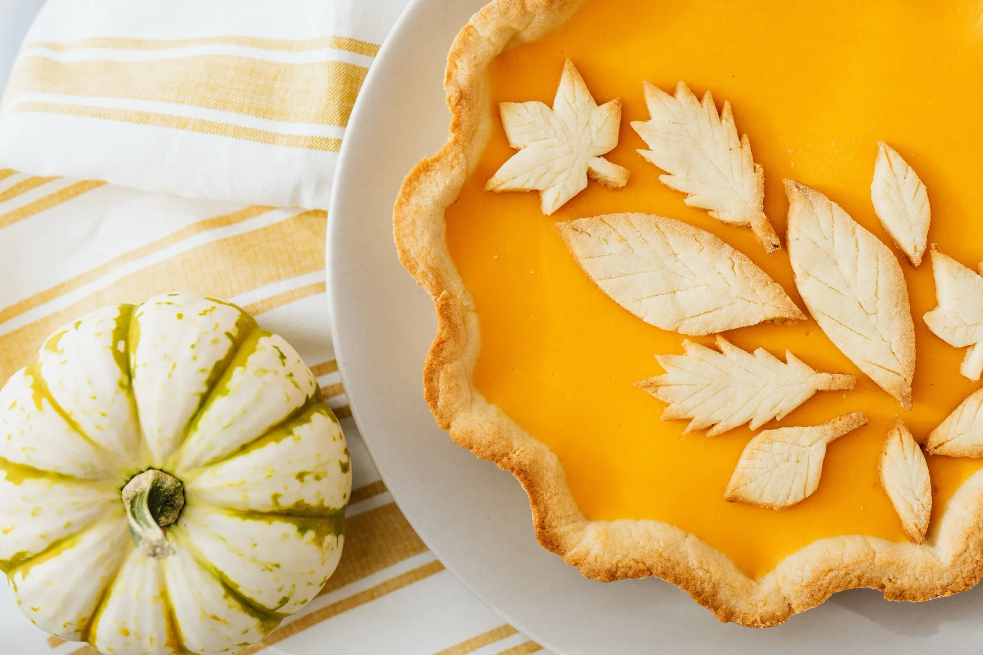 A pumpkin pie topped with pastry leaves beside a small white pumpkin