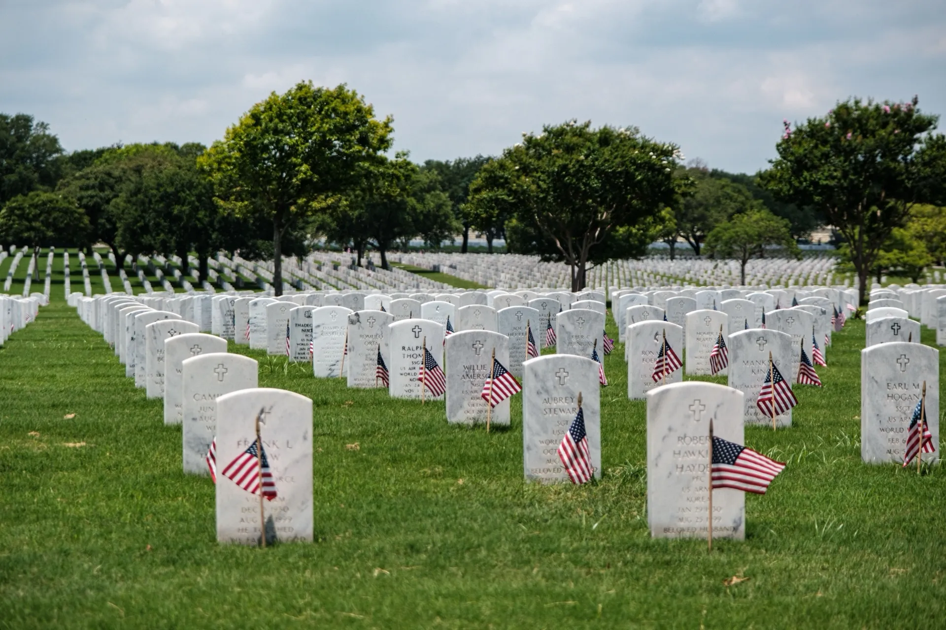 Rows of white headstones with small American flags in a military cemetery