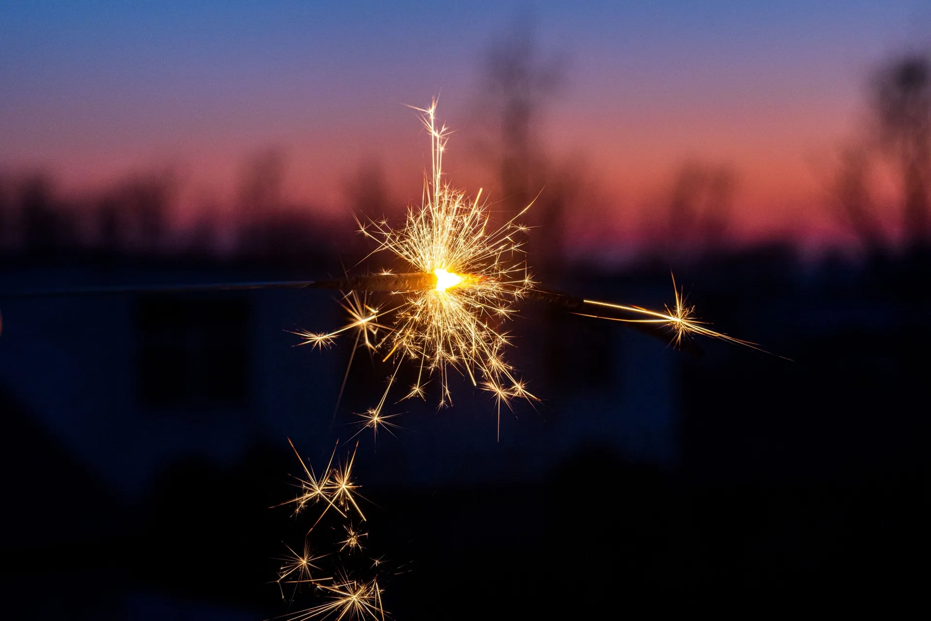 A lit sparkler against a pink and purple dusk sky
