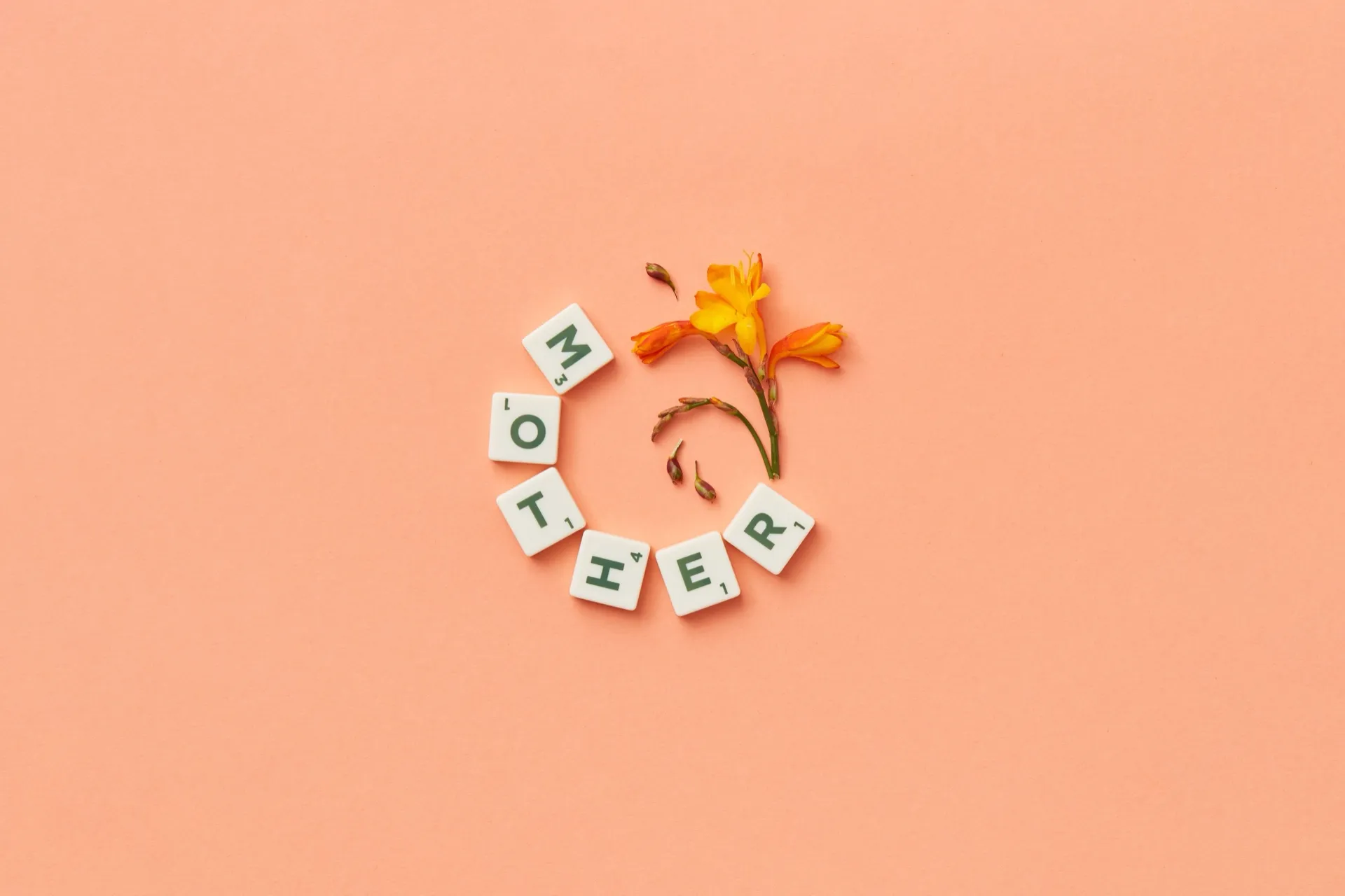 Letter tiles spelling Mother around an orange lily on a peach background