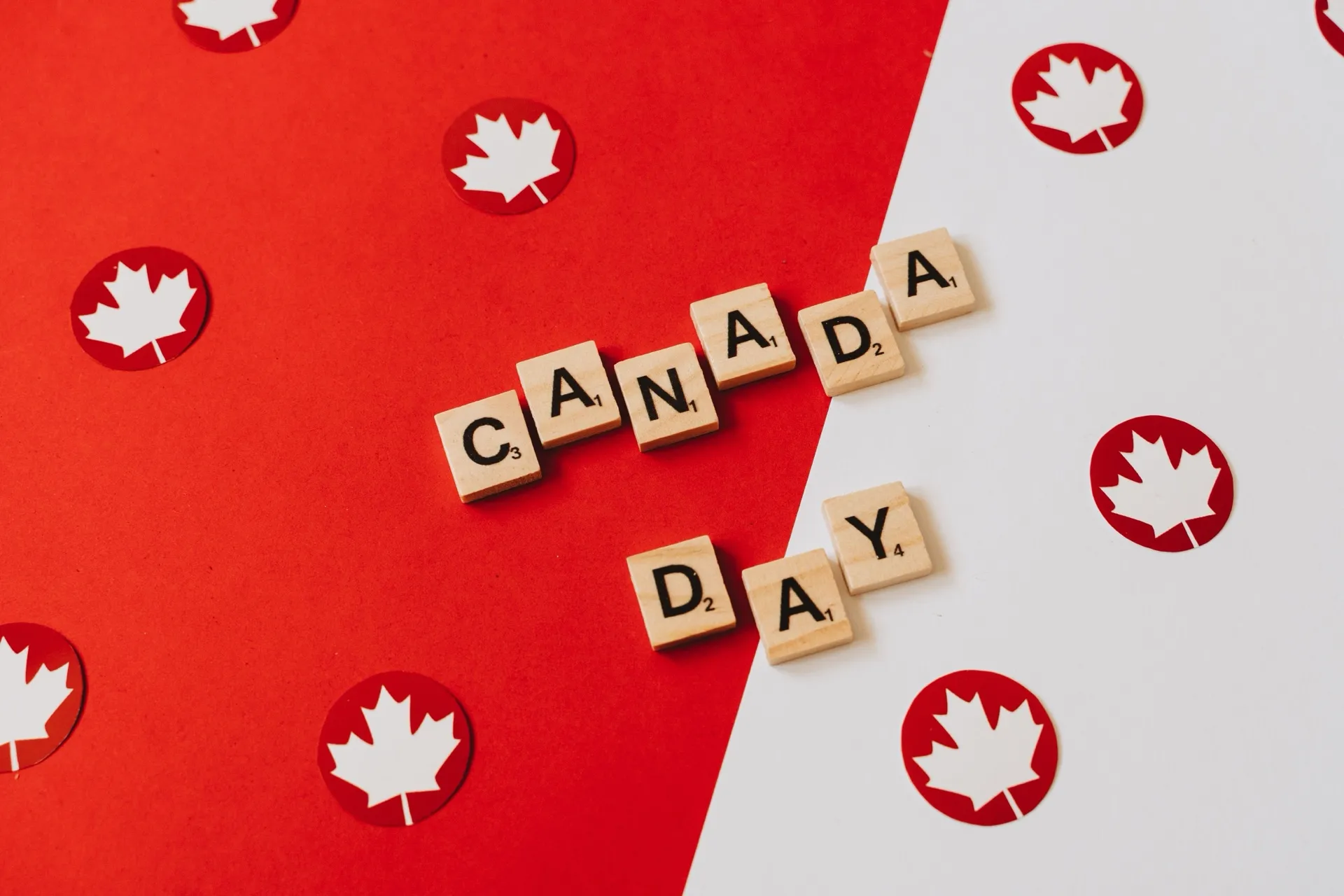 Letter tiles spelling Canada Day on red and white paper with maple leaf confetti