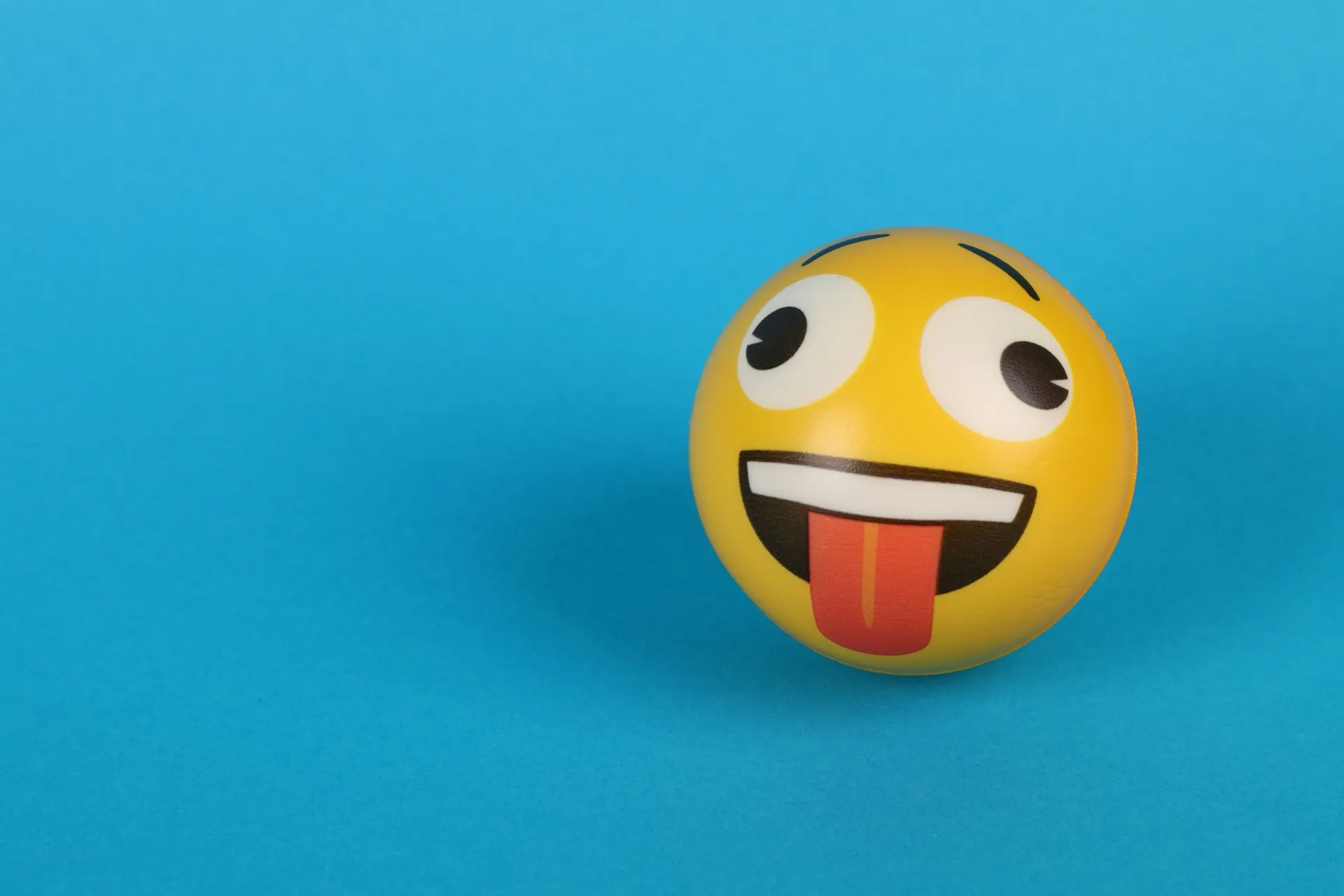 A goofy smiley face ball sticking its tongue out on a blue background